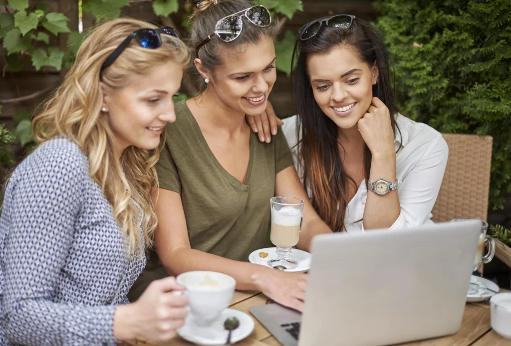 3 jeunes filles qui rigole et bois un café  devant un écran d'ordinateur 